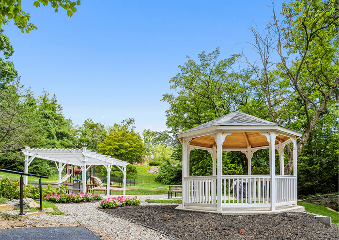 Charming garden view featuring a classic white gazebo and a pergola, surrounded by lush greenery and blooming flowers.