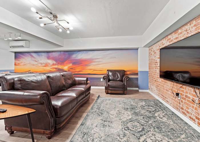 Charming living room with leather seating, a sunset mural, and a modern brick accent wall.