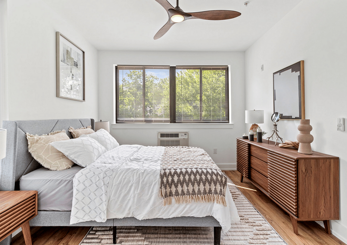 Bright bedroom with stylish decor, featuring a cozy bed, wooden accents, and large windows with natural light.