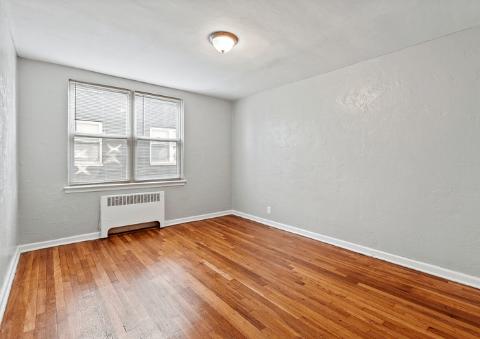 Bright, open room with polished hardwood floors and soft gray walls, featuring a large window for natural light.