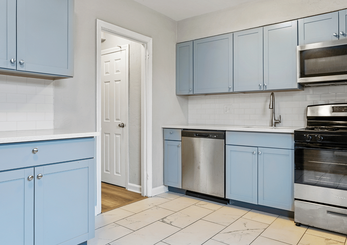 Bright kitchen with blue cabinets, stainless steel appliances, and sleek tiled flooring.