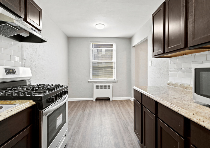 Modern kitchen with dark wood cabinets, granite countertops, and stainless steel appliances, showcasing a bright window and sleek flooring.