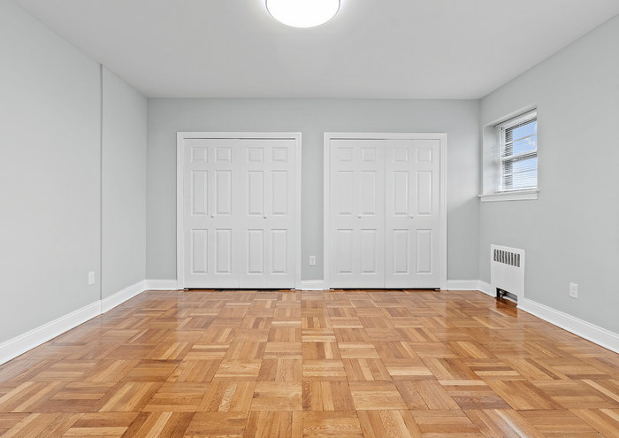 Bright and airy bedroom with elegant wooden flooring and dual white closets.