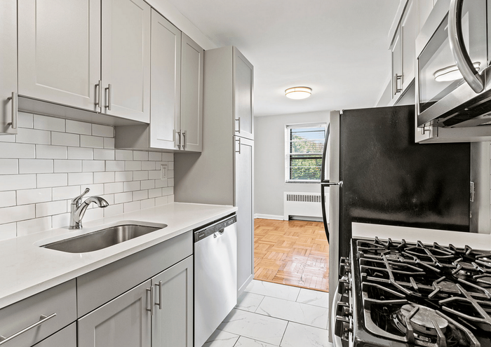 Modern kitchen with sleek white cabinets, stainless steel appliances, and large sunny window.