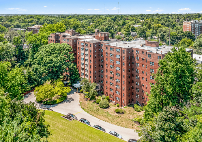 Aerial view of a large brick apartment building surrounded by lush greenery and a winding driveway.