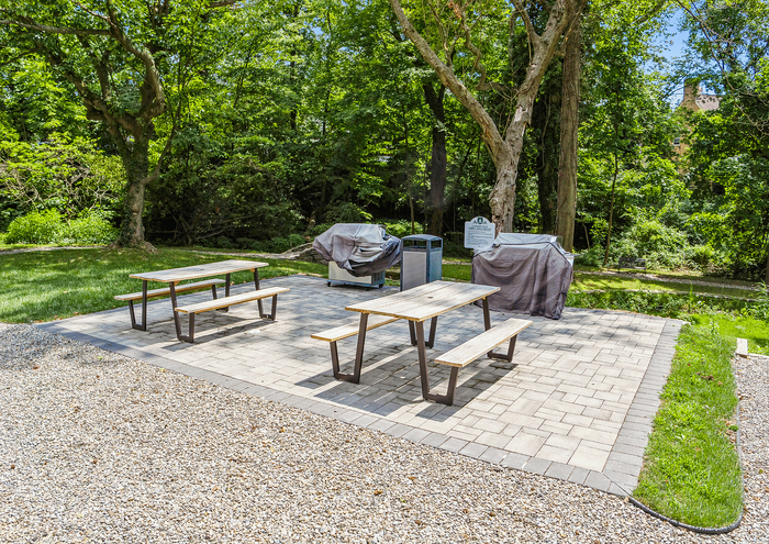 Charming outdoor picnic and BBQ area with wooden tables and lush greenery.