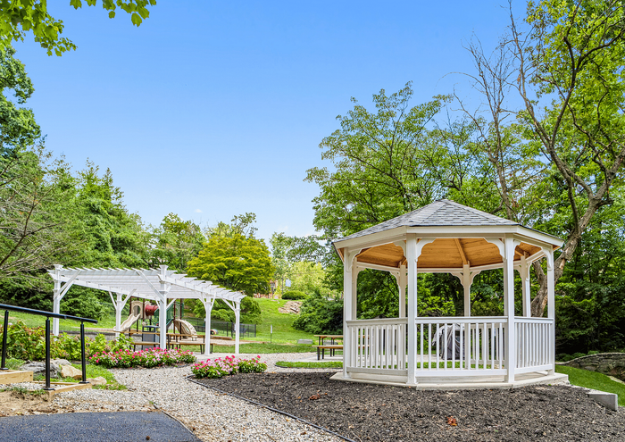 Charming garden with a white gazebo and pergola, surrounded by lush greenery and vibrant flowers.
