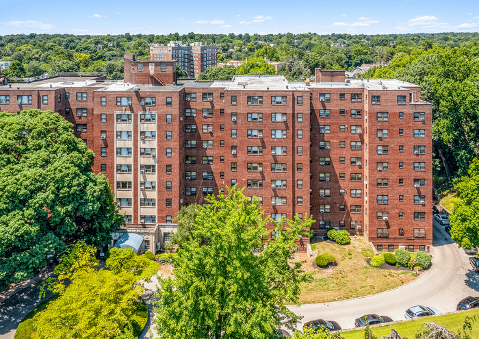Aerial view of a red-brick apartment building surrounded by lush greenery in a vibrant urban setting.