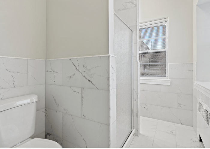 Chic bathroom featuring marble tiles, a modern toilet, and a window with natural light.
