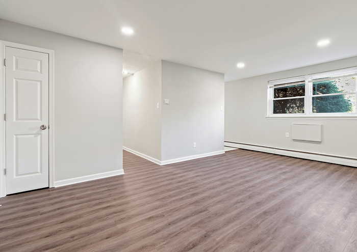Spacious room with large window, wooden floors, and white walls, ideal for customizable living.