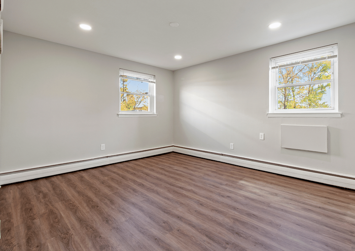 Spacious corner room with hardwood floors and large windows, welcoming natural light.