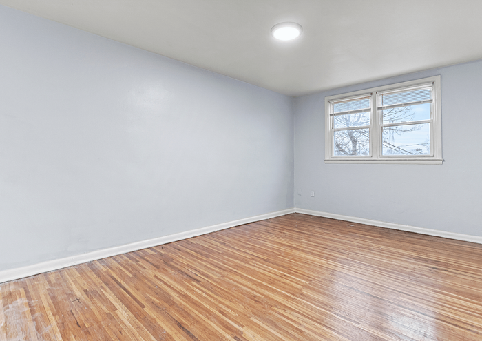 Bright, empty room with hardwood floors and a large window allowing natural light.