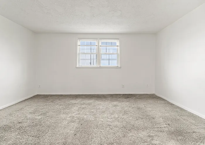 Inviting room with a large window providing abundant natural light and soft carpet flooring.