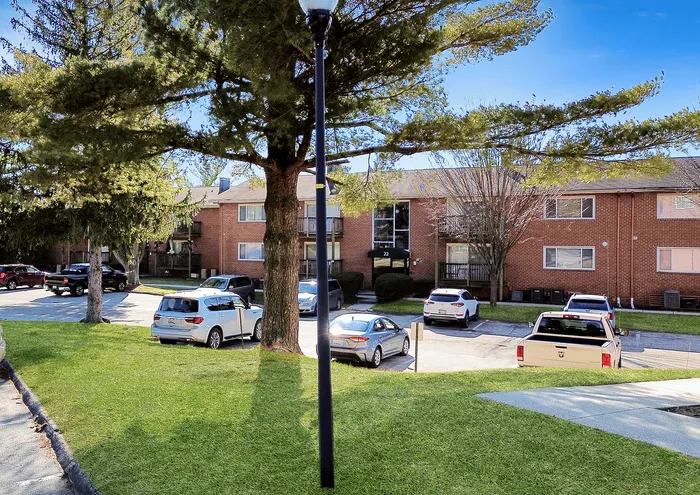 Bright sunny day at a well-maintained apartment complex with brick buildings and lush green surroundings.