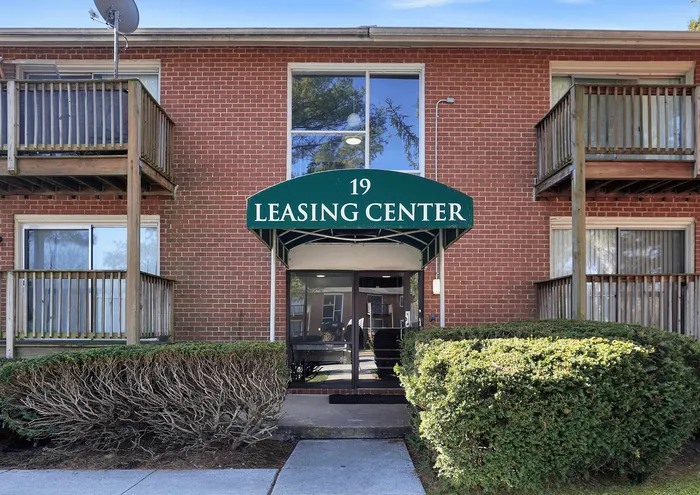 Inviting entrance to the leasing center of a brick apartment building with green awning.