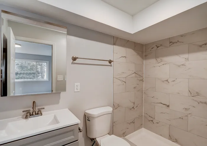 Contemporary bathroom featuring elegant marble tiles, a stylish vanity, and a bright window view.