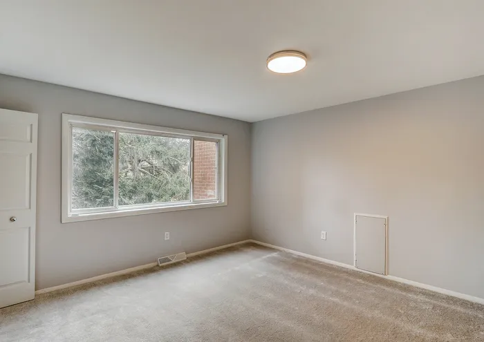 Inviting empty bedroom with a large window and soft carpeting.