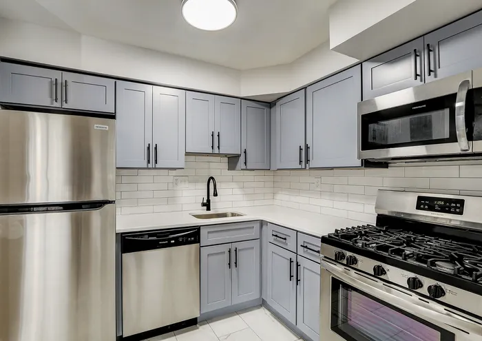Modern kitchen with stainless steel appliances, gray cabinetry, and clean white subway tiles.