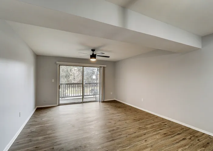 Spacious empty living room with hardwood floors, large sliding glass door, and ceiling fan.