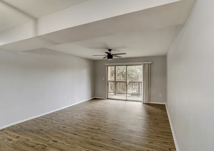 Spacious living room featuring hardwood floors, a ceiling fan, and large sliding glass doors leading to a balcony.