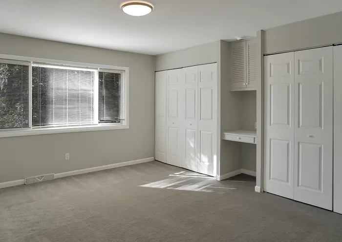 Inviting bedroom with natural light, grey carpet, large closets, and sleek window blinds.