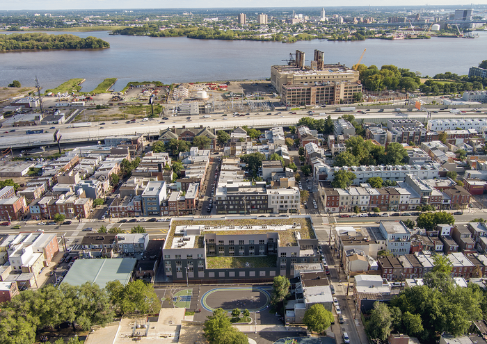 Aerial view of a vibrant urban neighborhood near a river, featuring modern architecture and lush greenery.