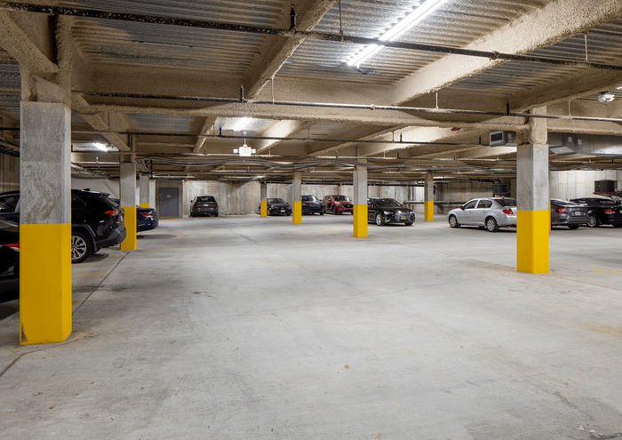 Spacious underground parking garage with multiple cars parked in well-lit spaces and yellow safety pillars.