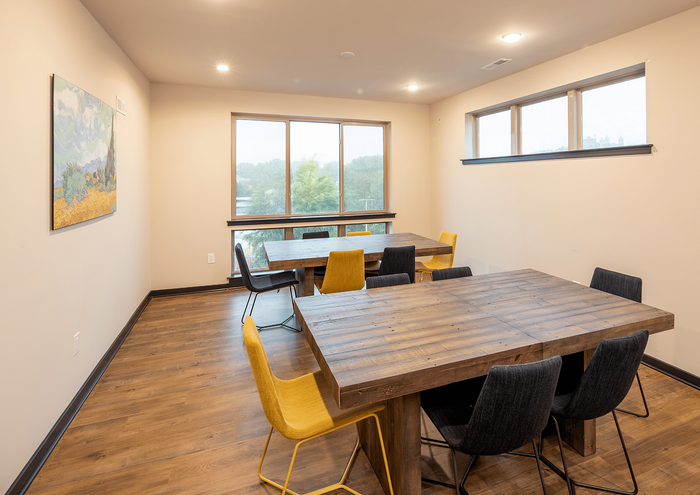 Bright, spacious dining room with modern wooden tables, yellow and black chairs, and large windows offering natural light.
