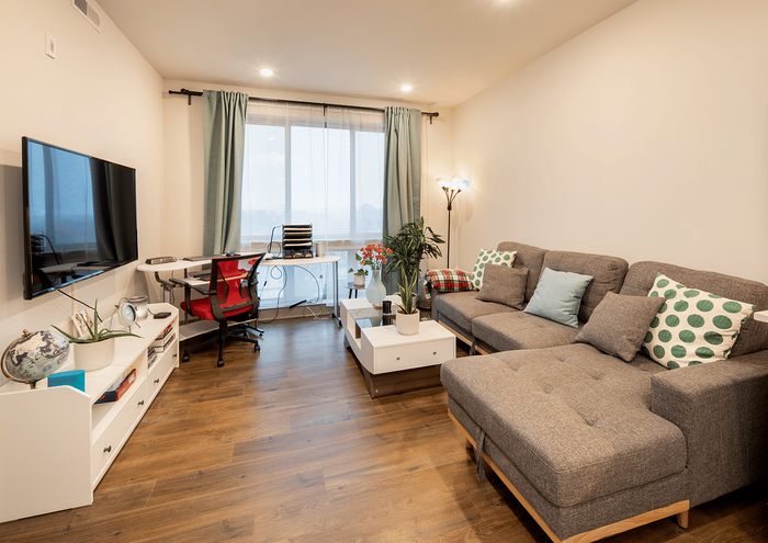Cozy living room with modern gray sectional sofa, stylish decor, and a workspace, enhanced by warm lighting and wood floors.