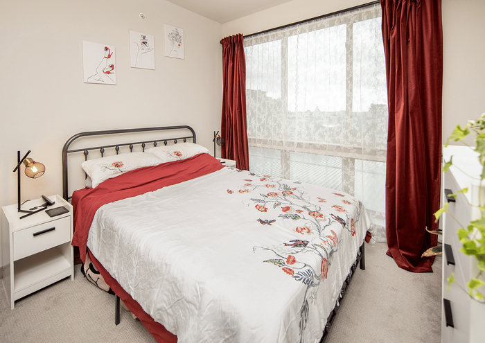 Inviting bedroom with a stylish metal bedframe, red accents, and large window with red curtains.
