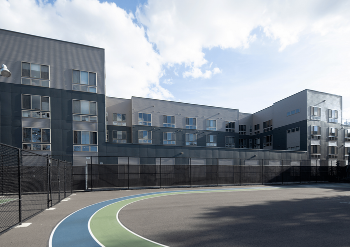 Modern apartment complex with sleek design and large windows, adjacent to a multi-colored running track.