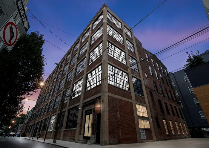 Street view of a historic urban loft building with large industrial windows against a twilight sky.