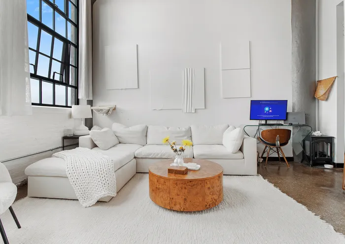 Bright and stylish modern living room with large windows, white sofa, and a wooden coffee table.