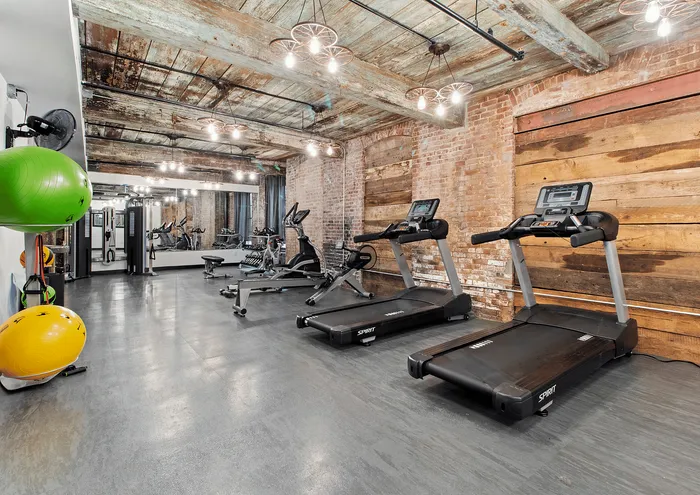 Rustic gym with modern equipment, including treadmills and exercise balls, under distressed wood ceilings.