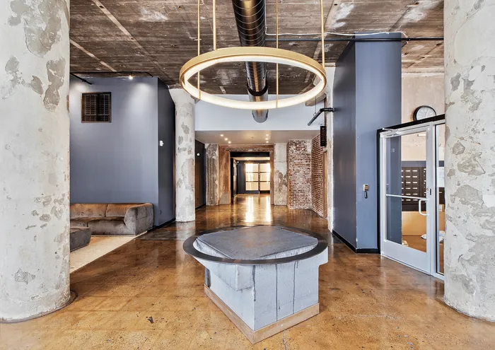 Contemporary apartment lobby featuring industrial design with exposed concrete pillars and modern lighting.