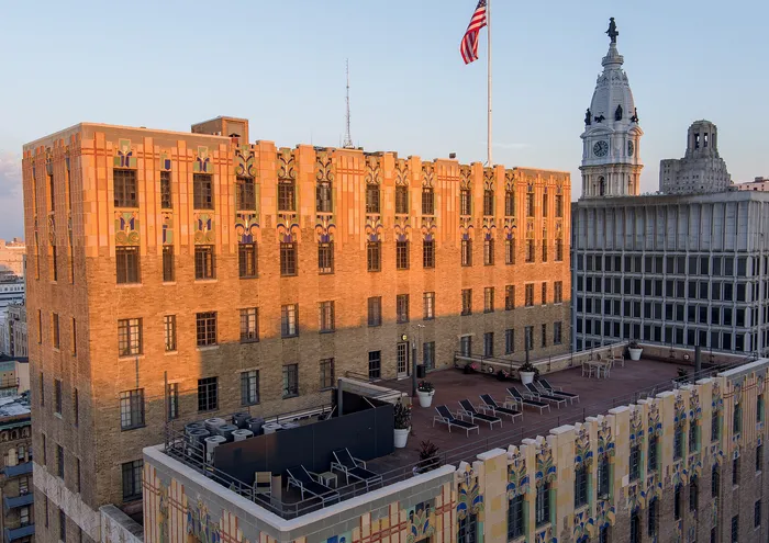 Elegant historic building with a rooftop terrace and American flag, set against a city skyline at sunset.