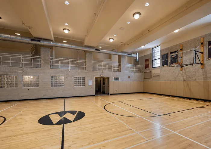 Bright and spacious indoor gymnasium with hardwood flooring, basketball hoops, and high ceilings.