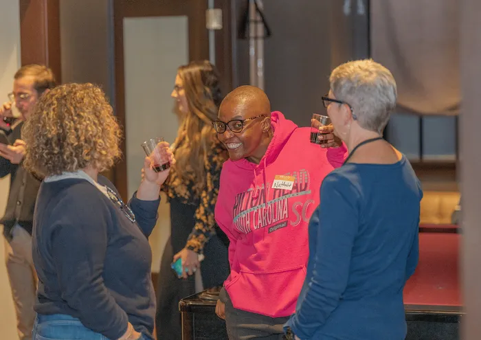 A lively group of people enjoying a social event, smiling and holding drinks.