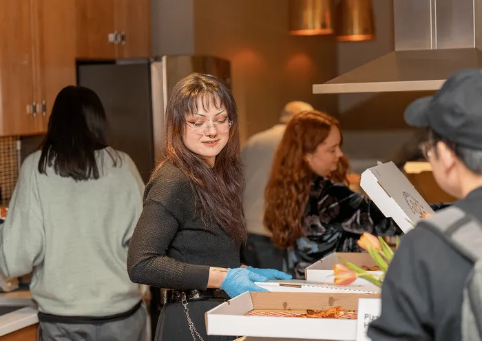 Community gathering in a modern kitchen with people enjoying pizza.