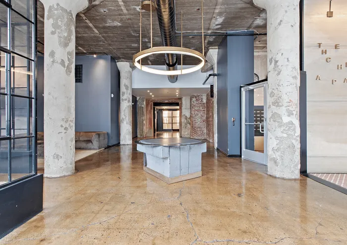 Urban apartment lobby featuring polished concrete floors, rustic pillars, and modern light fixture.