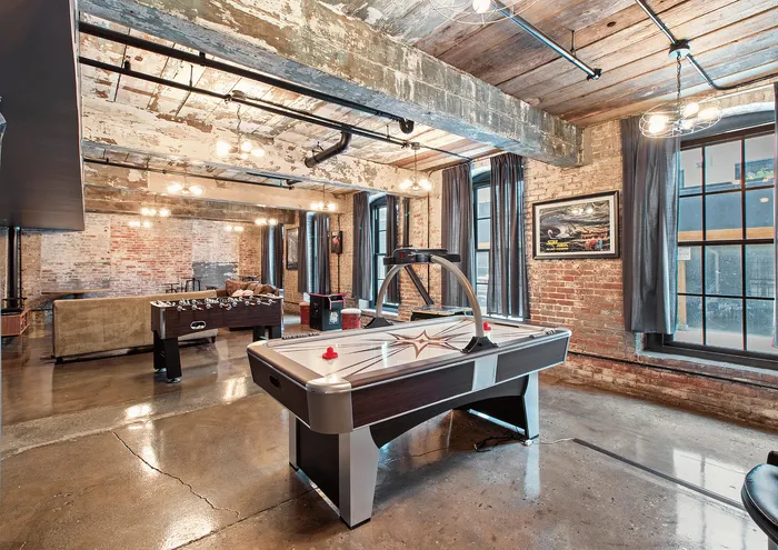 Chic industrial game room with air hockey and foosball tables, featuring exposed brick walls and wooden beams.