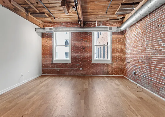 Stylish industrial loft with exposed brick walls, wooden ceiling beams, and large windows.
