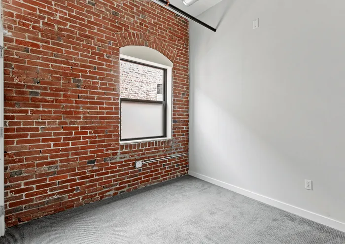 Charming room with exposed brick wall and arched window, combining rustic elegance and contemporary style.