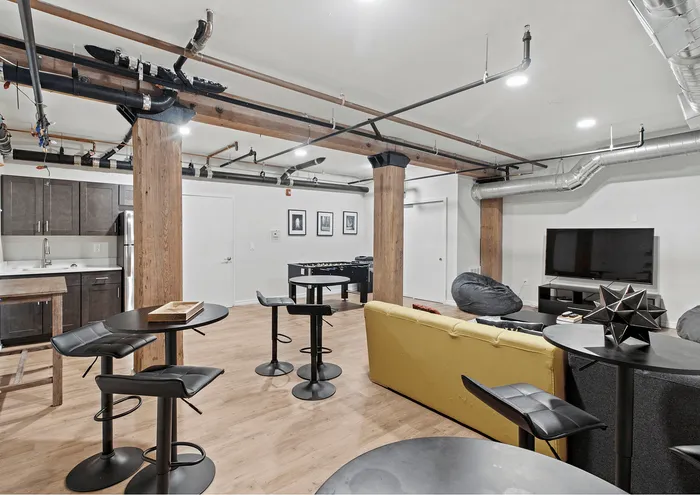 Stylish loft with exposed pipes and beams, featuring a cozy seating area, modern kitchen, and entertainment setup.