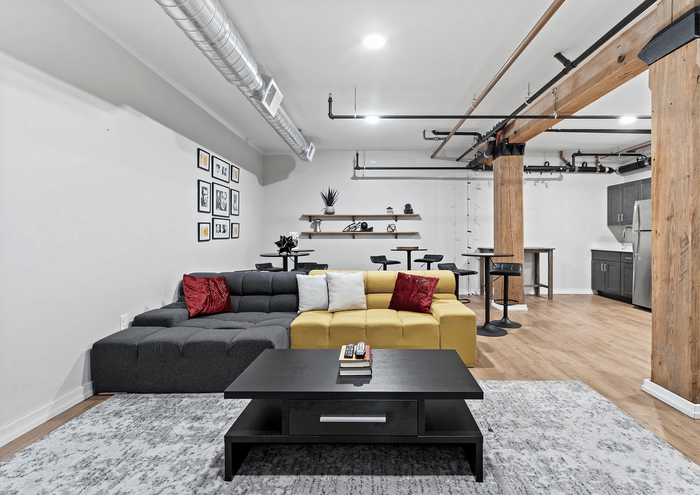 Spacious loft with modern industrial design, featuring a stylish sectional sofa in a bright living area, exposed wooden beams, and a sleek kitchen.