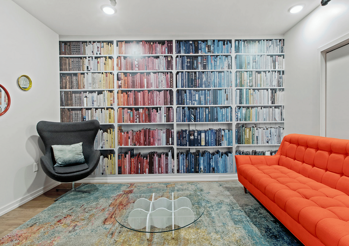 Bright and modern room featuring a colorful bookshelf mural, a cozy dark chair, and a bold orange couch.