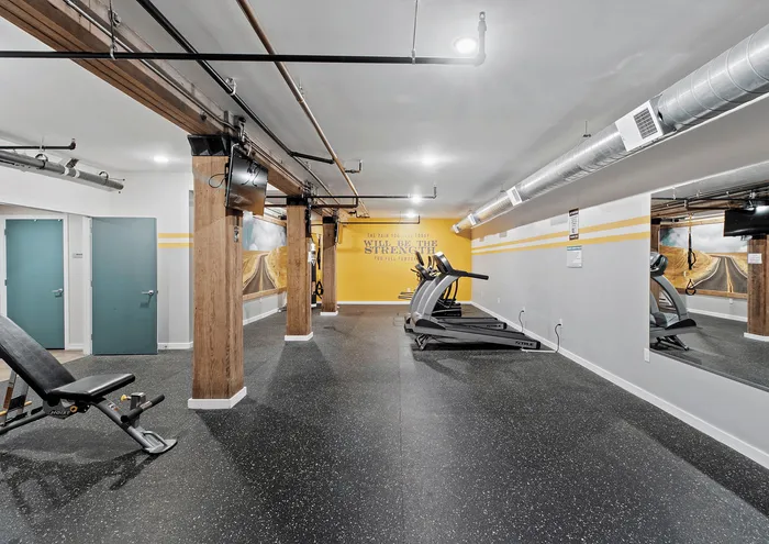 Modern gym interior with treadmills, bench, and motivational wall art.