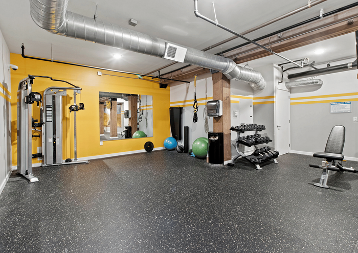 Modern fitness room with exercise equipment, weights, and bright yellow accent wall.