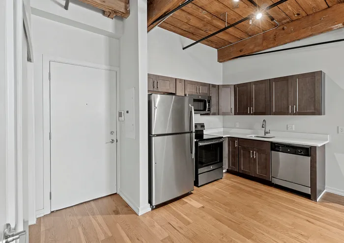 Modern kitchen with stainless steel appliances, wooden cabinetry, and exposed beam ceiling.
