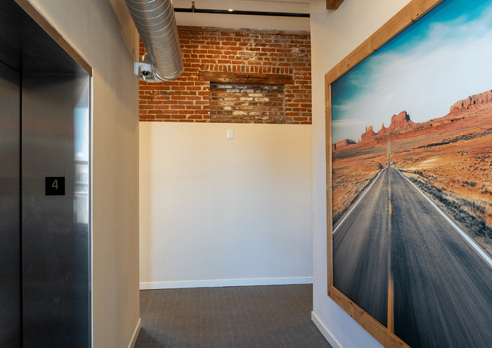 Stylish modern hallway with exposed brick wall, large scenic artwork, and elevator access.